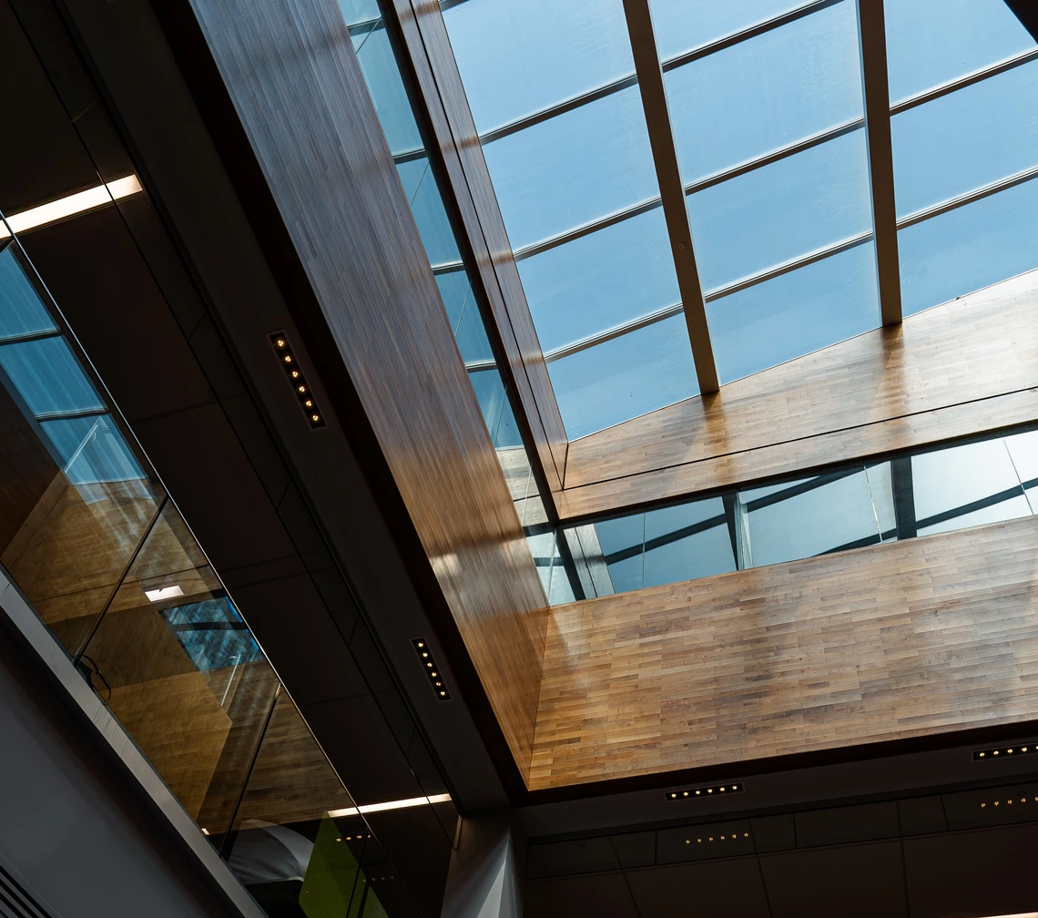 Interior of a building with natural light coming through a large glass skylight and wooden ceiling panels.
